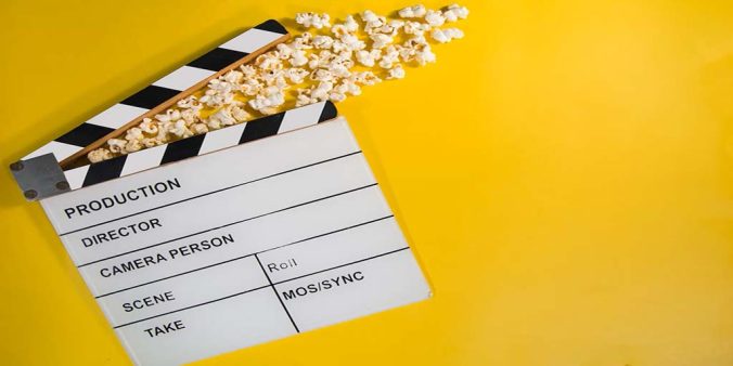 Image of a black and white clapper board laying on a yellow background with popcorn